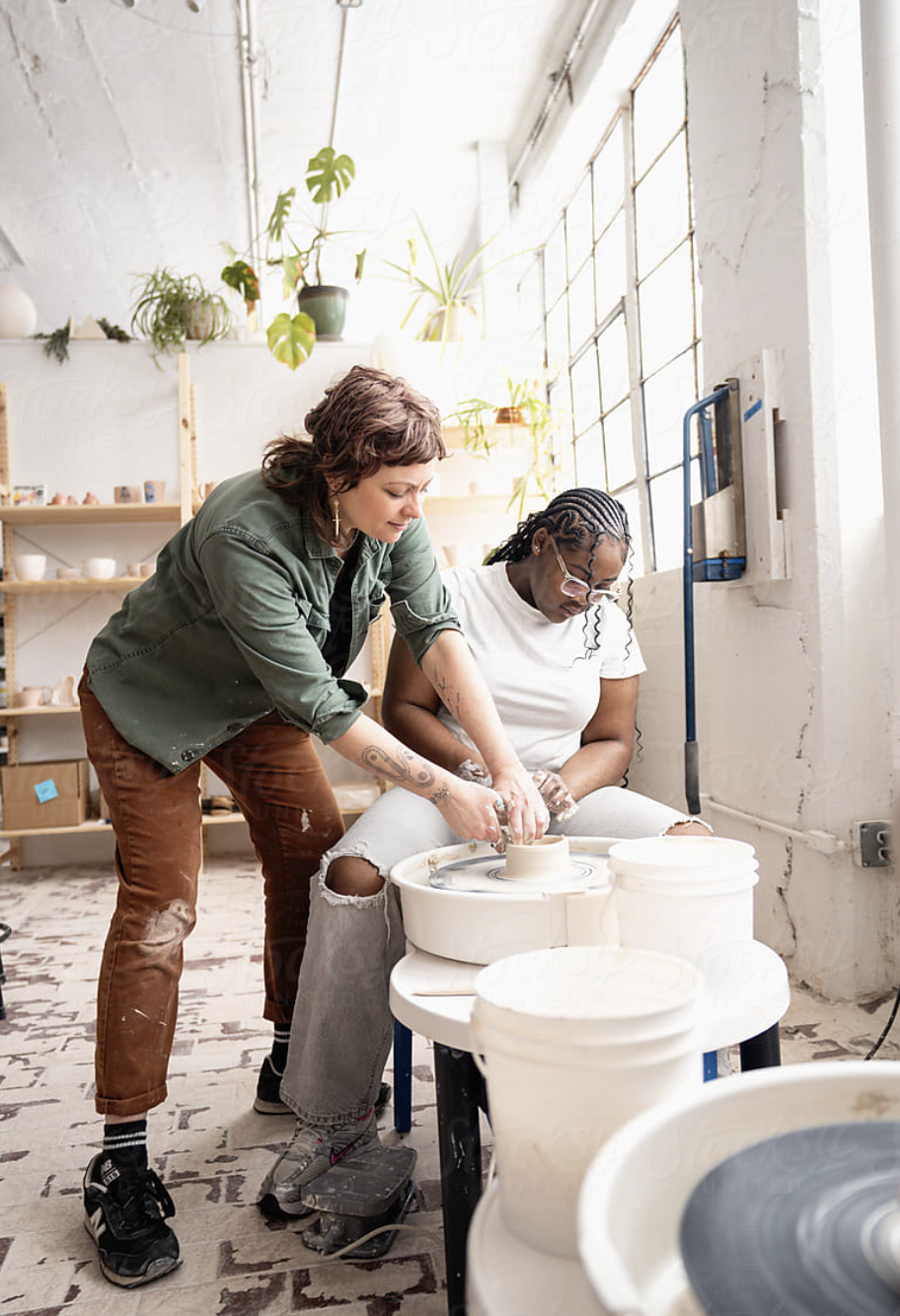An instructor guiding a beginner shaping clay on a pottery wheel